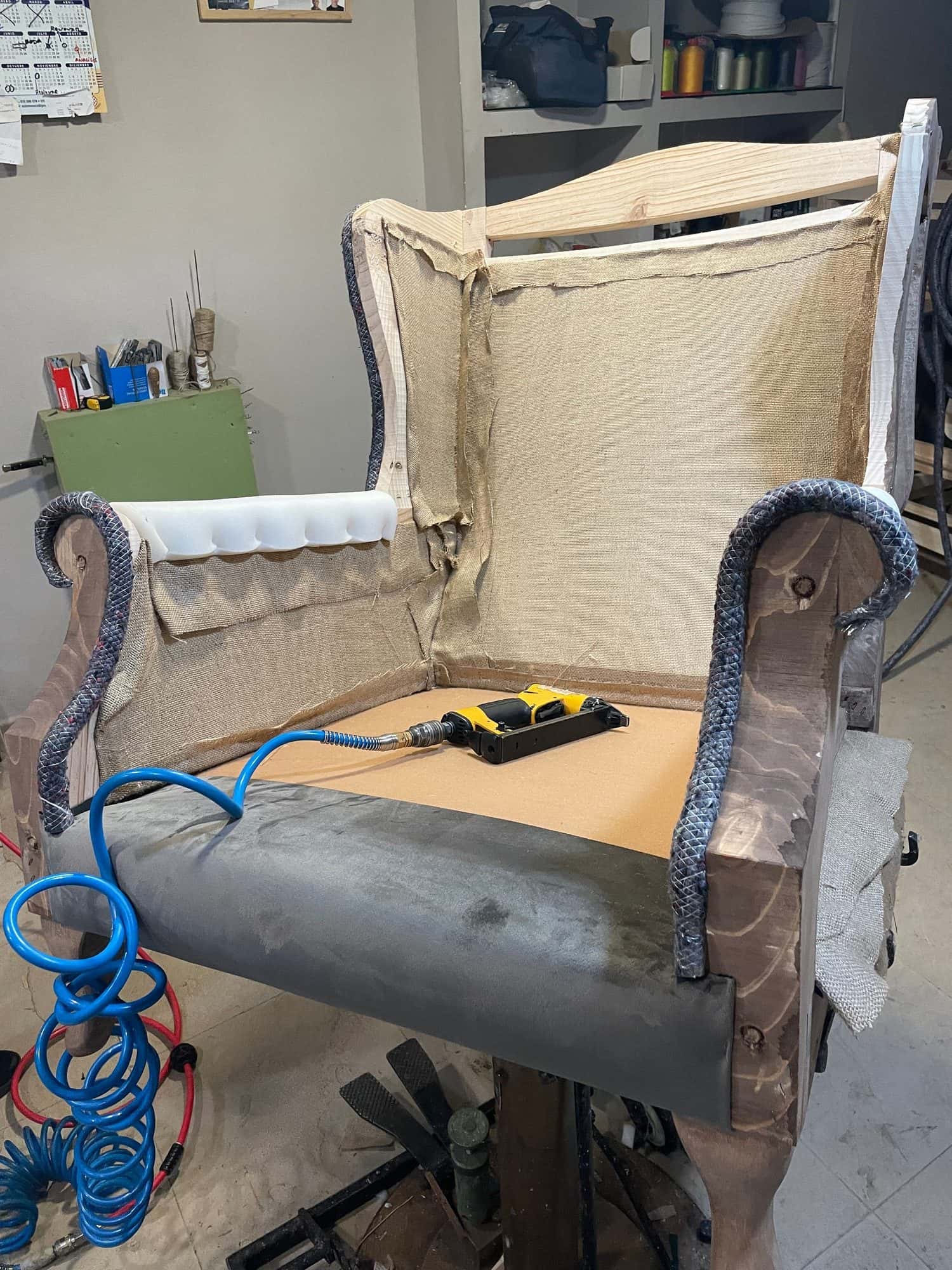 Sillón orejero en proceso de tapizado sobre el caballete del taller