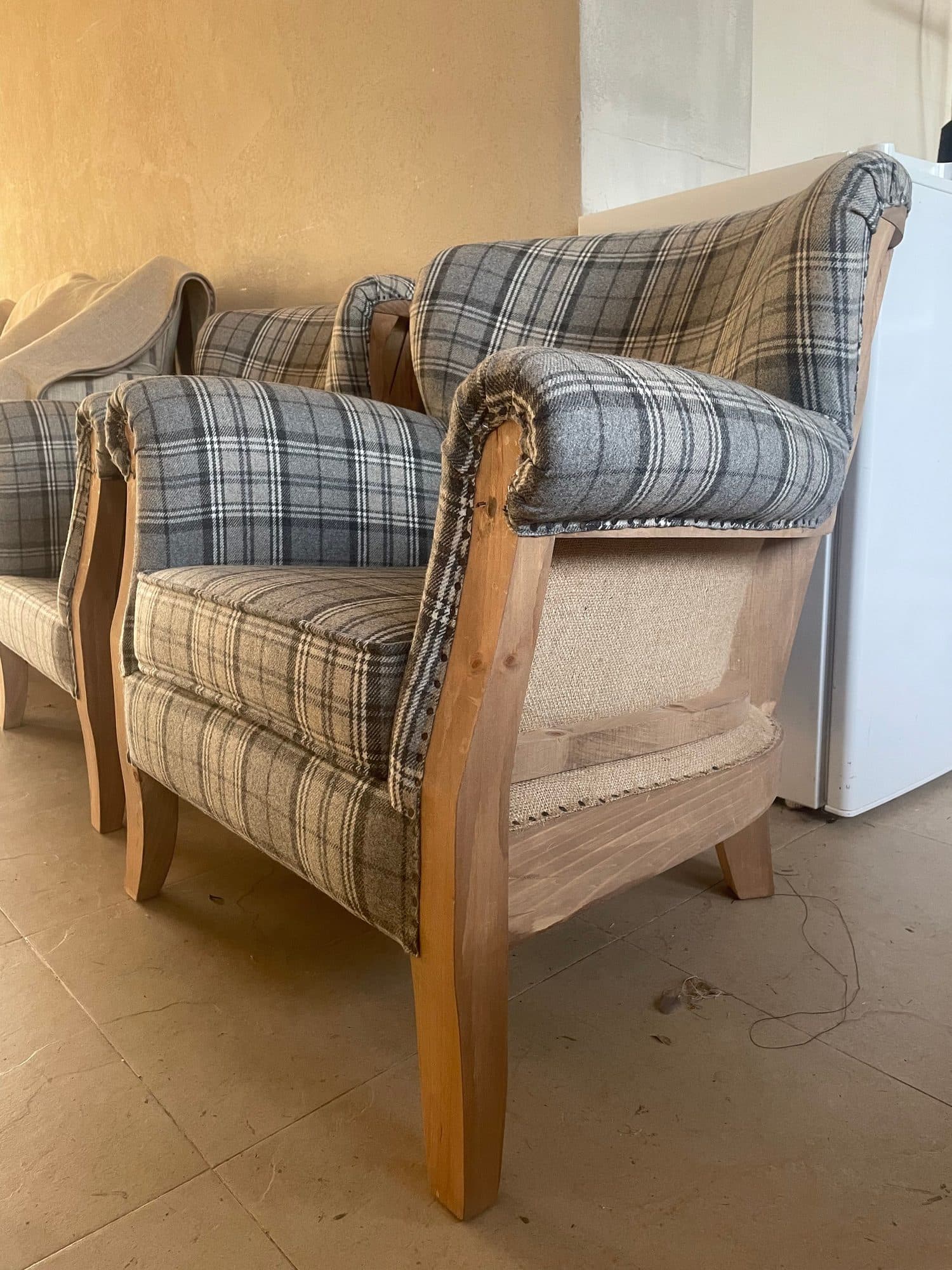 Butacas tapizadas en tejido de cuadros, una de ellas todavía en proceso con la estructura visible