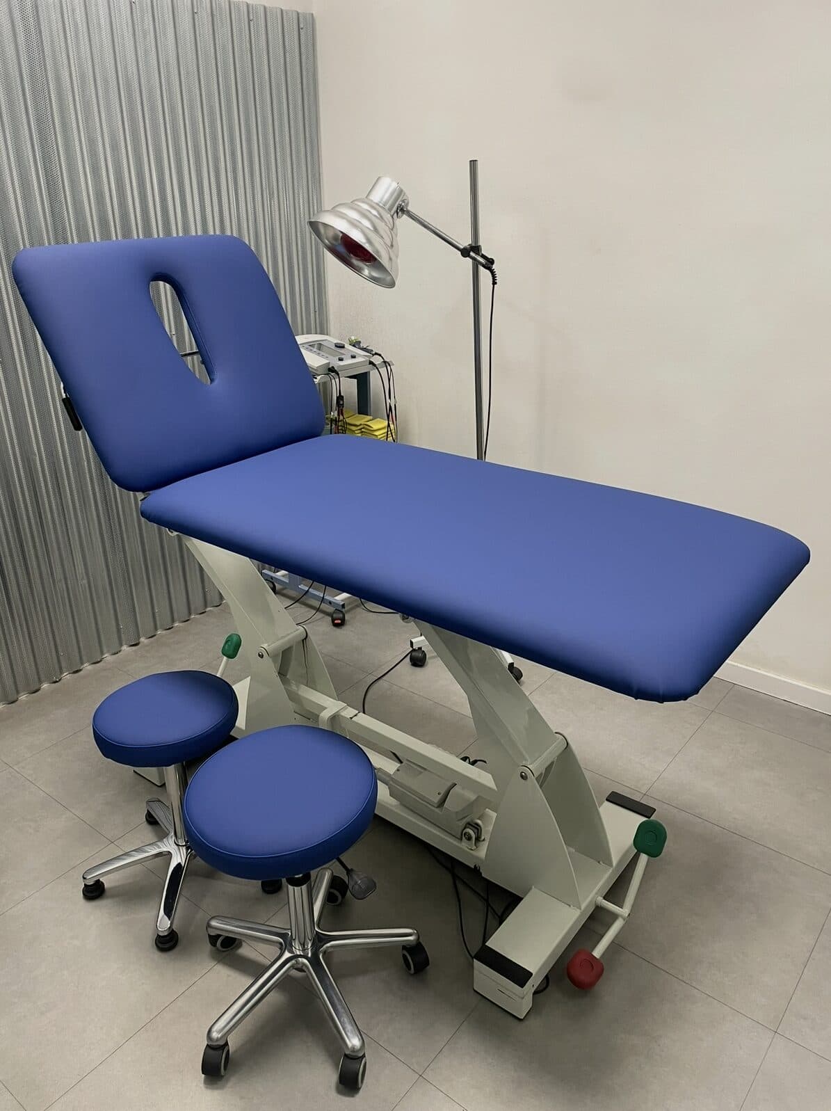 Camilla de rehabilitación con orificio facial y dos taburetes retapizados en azul en un centro de fisioterapia