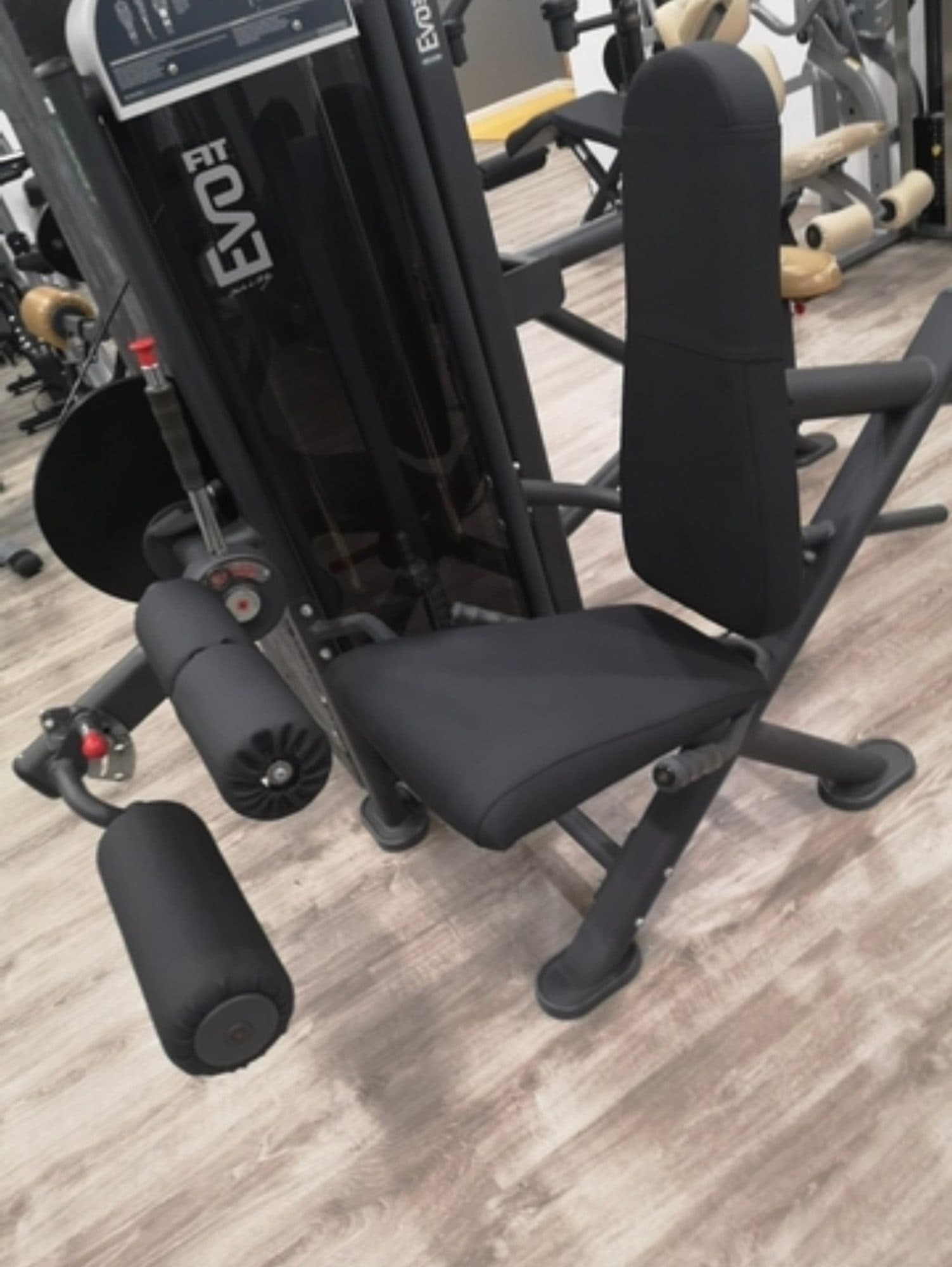 Máquina de gimnasio con asiento, respaldo y rodillos tapizados en negro