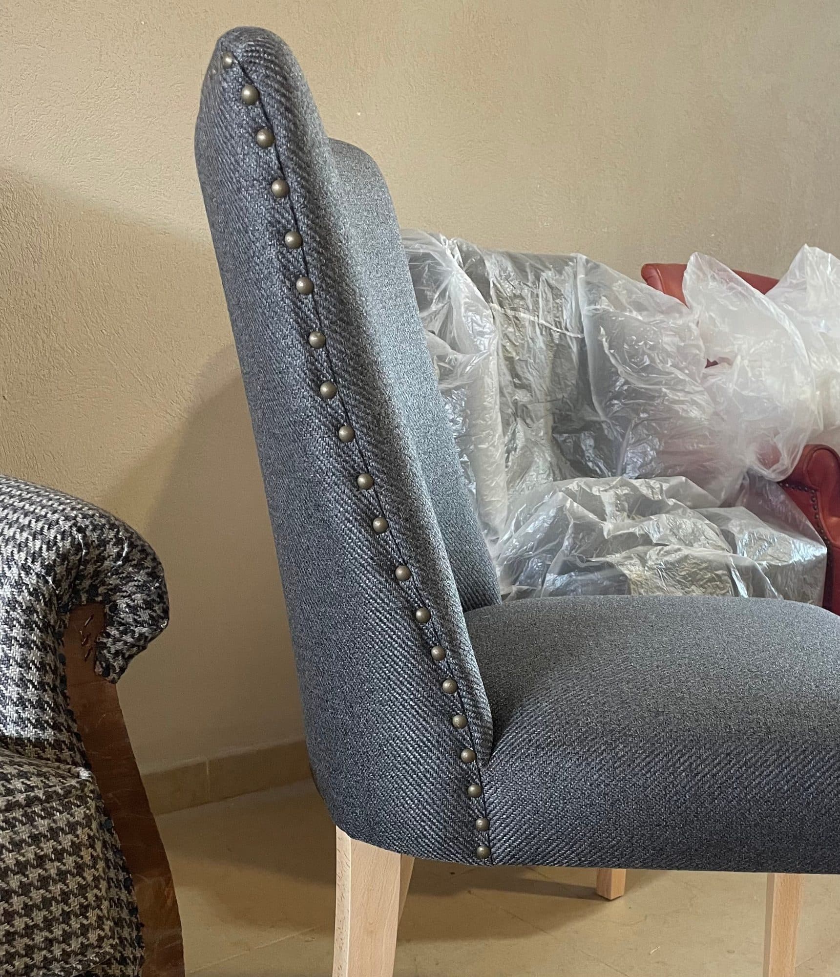 Silla tapizada en tejido gris con remate de tachuelas alineadas