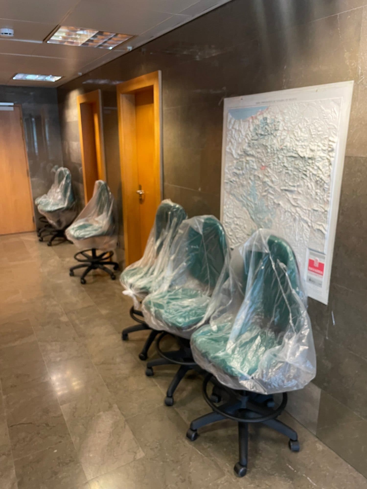 Sillas de oficina protegidas con plástico alineadas en un pasillo antes de su colocación