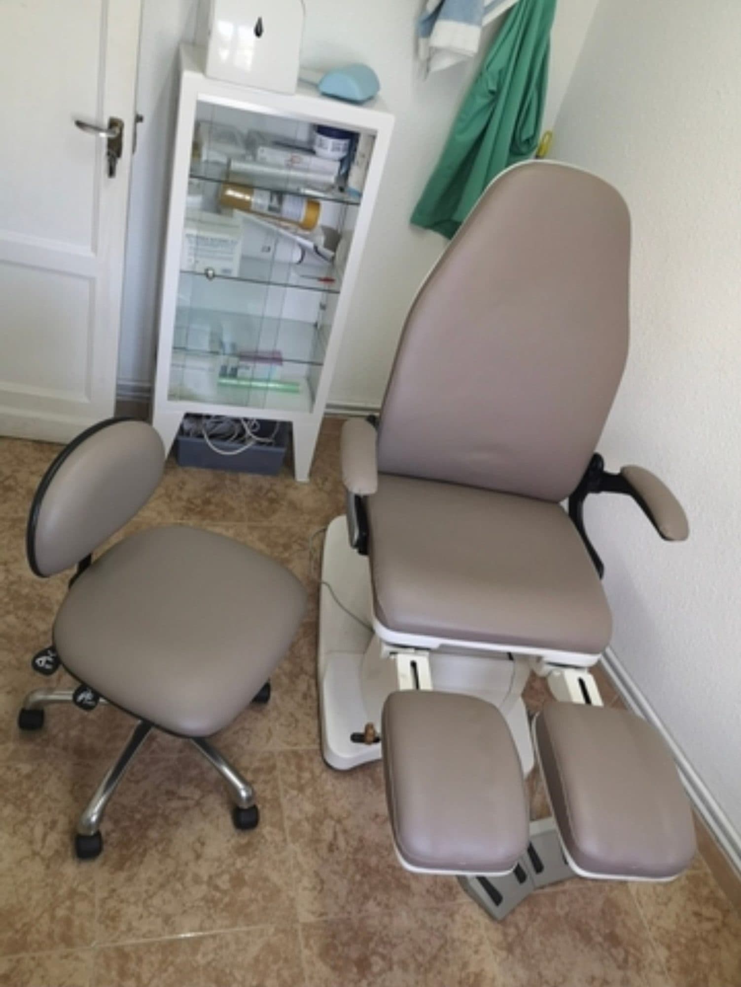 Sillón de podología y taburete tapizados en gris en una consulta