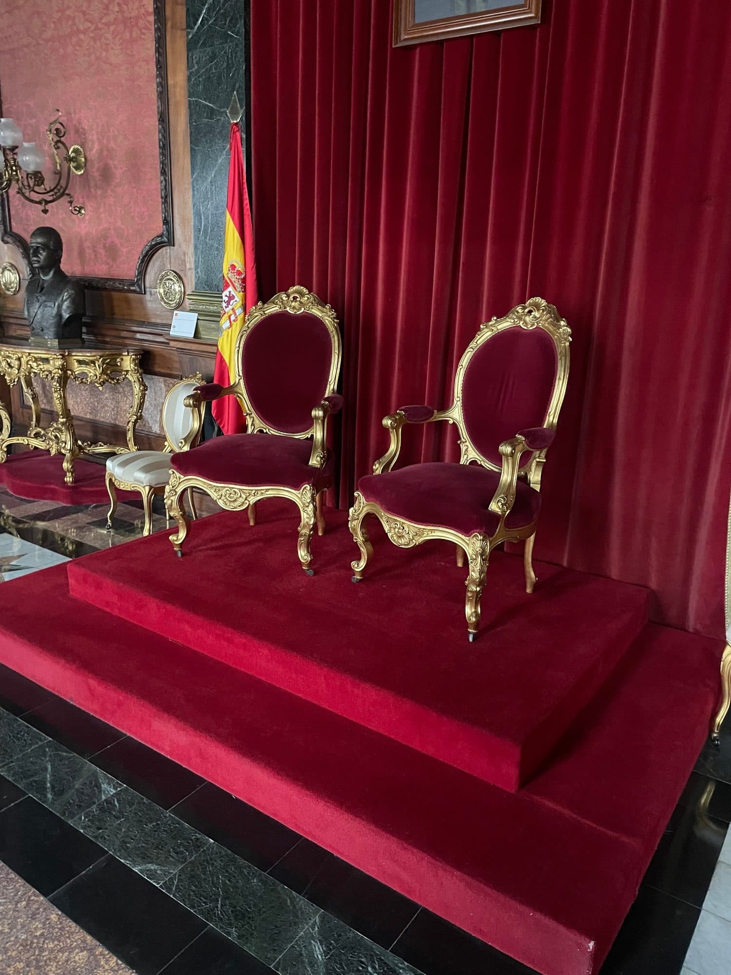 Pareja de sillones clásicos de madera dorada tapizados en terciopelo rojo en un salón de protocolo