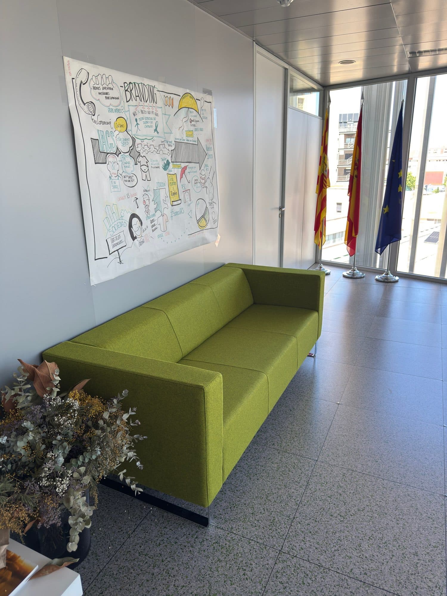 Sofá tapizado en verde en el vestíbulo de un edificio institucional con banderas
